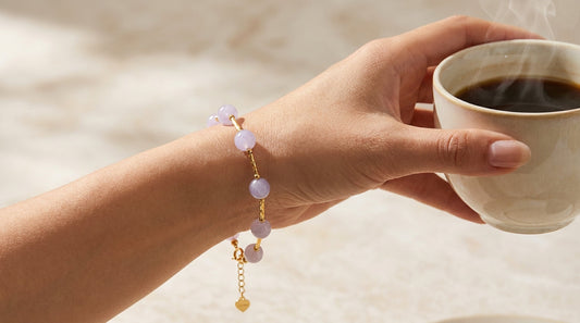 a close up image of a woman's hand with a purple jade bracelet, holding a cup of coffee